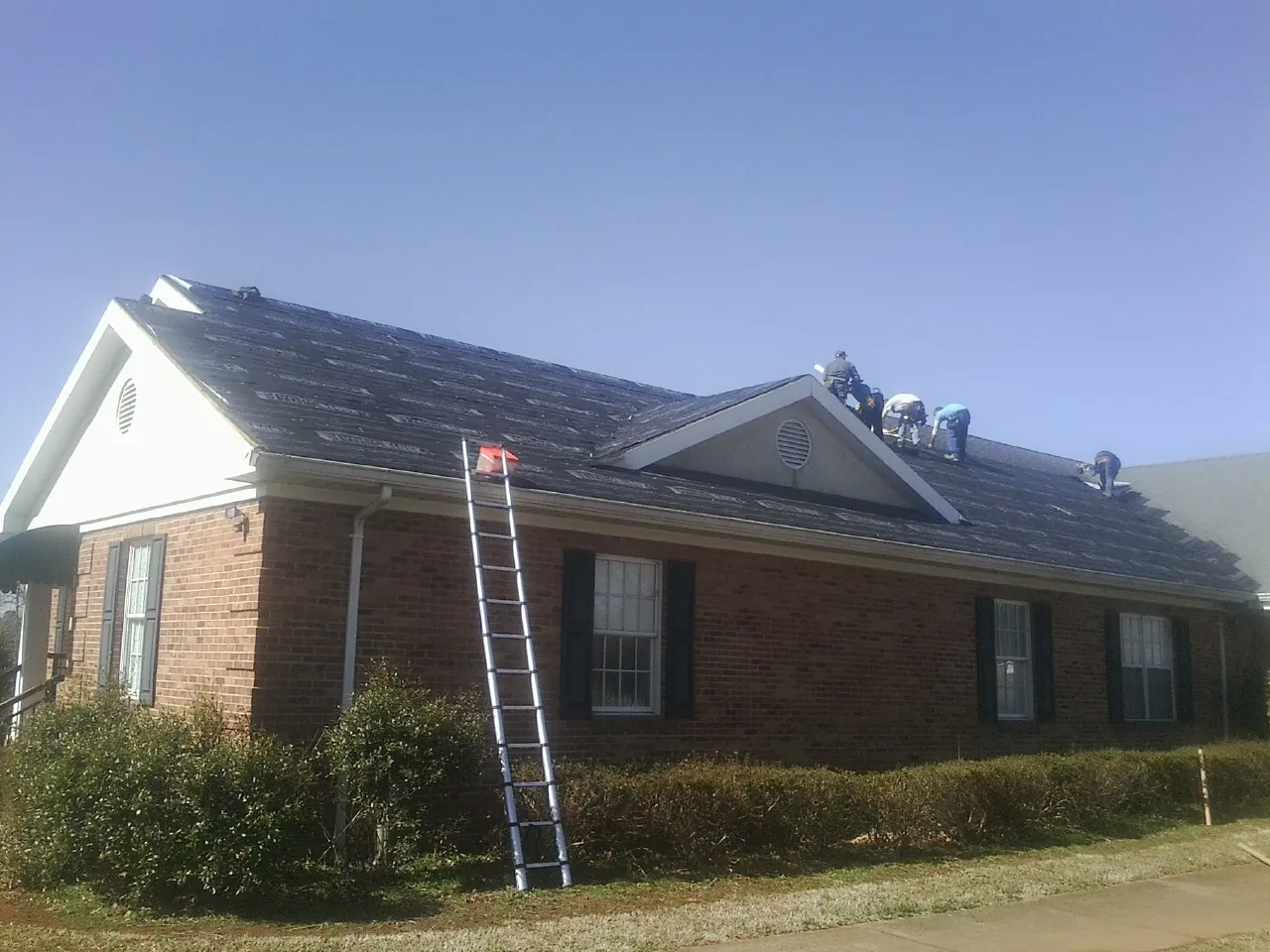 Crew tearing shingles off a brick ranch roof with a ladder set — Metal Roof Repair work by our crew in Highspire