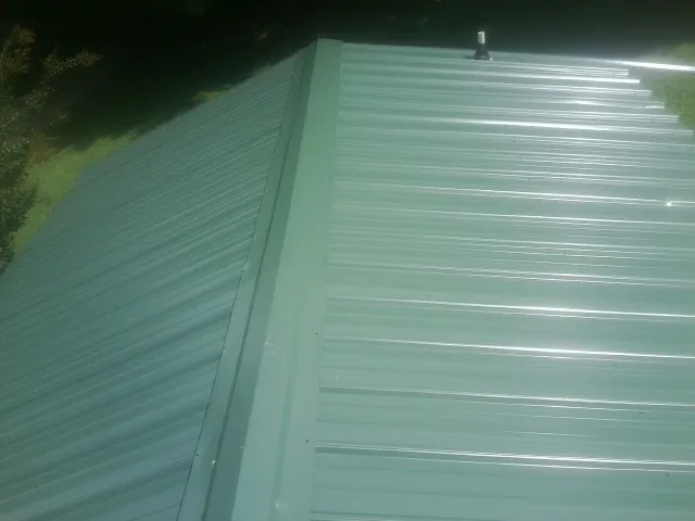 New green metal panels meeting at the ridge of a roof — Flat Roof Repair work by our crew in Highspire