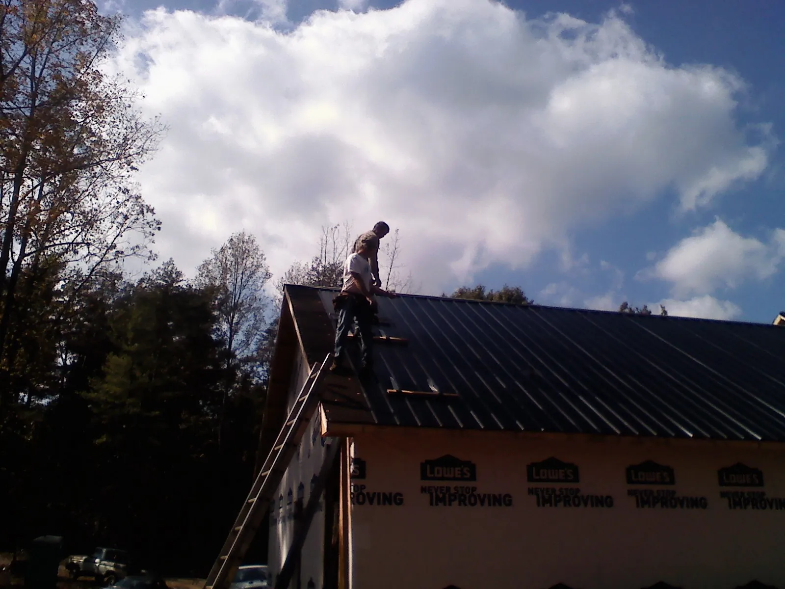 Roofer fastening dark metal panels high against a cloudy sky, from a Roof Inspection job in Highspire