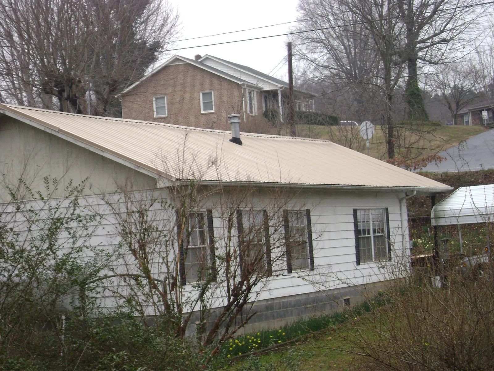 Tan metal roof on a white sided house set into a hillside — Commercial Roofing by Roofing Brothers in Highspire